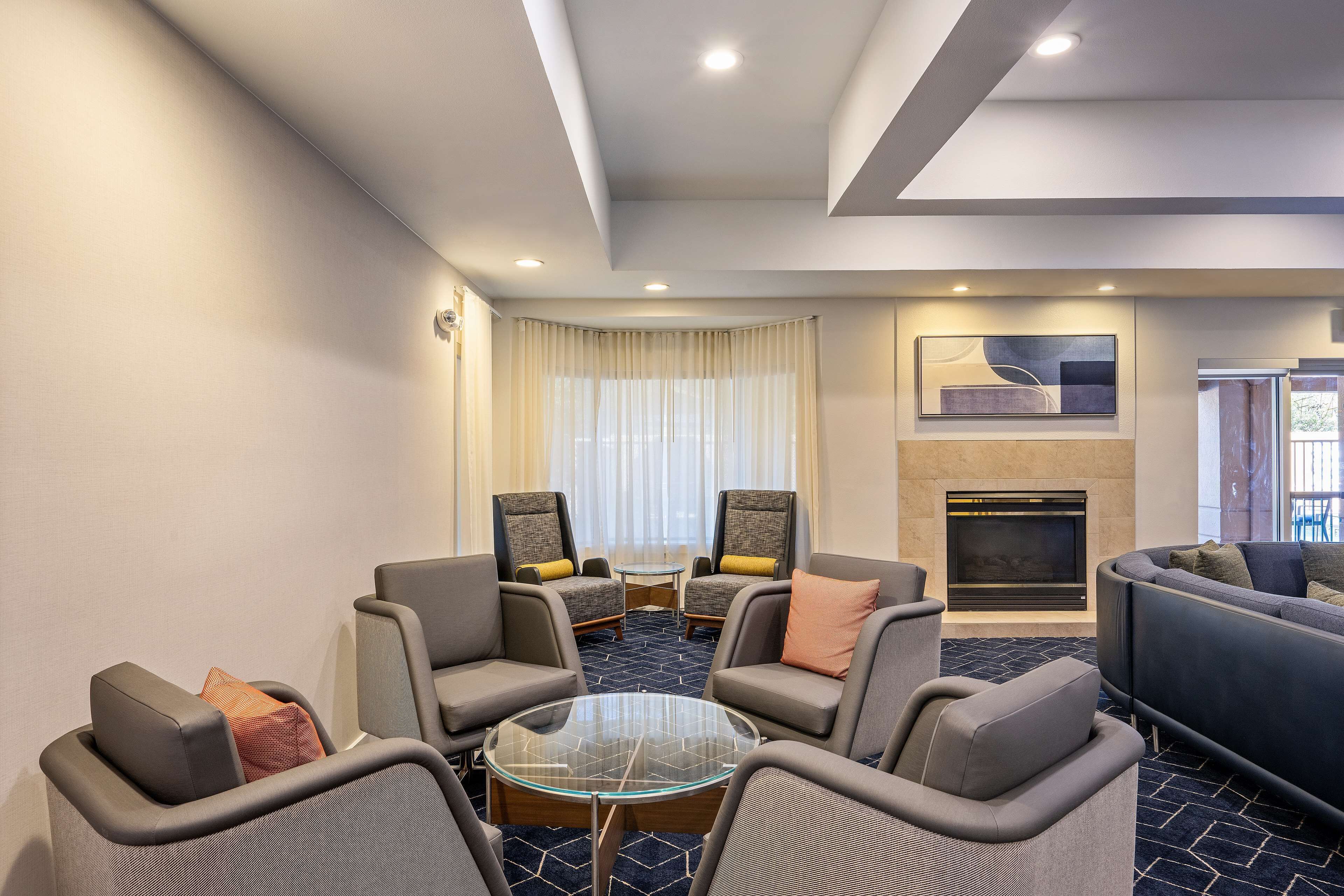 A modern hotel lobby with a seating area, a fireplace, and a large window with curtains.