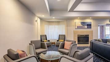 A modern hotel lobby with a seating area, a fireplace, and a large window with curtains.