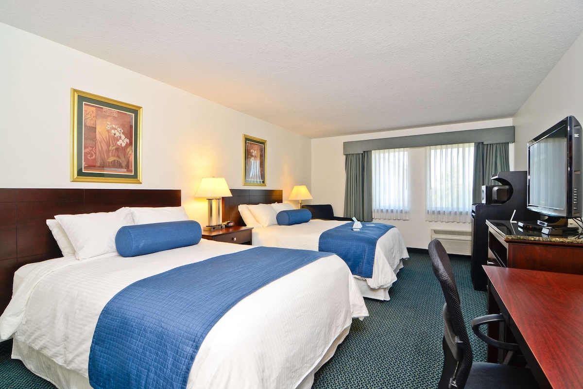 A hotel room with two beds, a desk, a television, and a window with curtains.