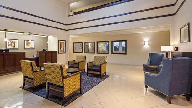 A hotel lobby with a reception desk, seating area with patterned chairs, a blue sofa, and framed artwork on the walls. - Best Western Gas City (Gas City)