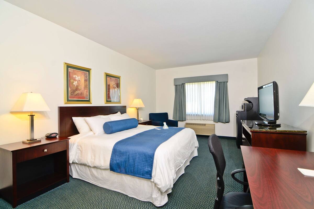 A hotel room with a bed, two bedside lamps, a desk with a television, and a window with curtains.
