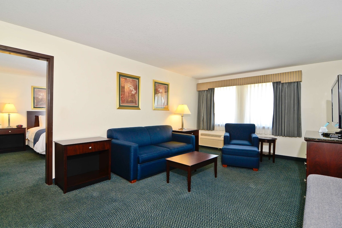 A hotel room with a bed, a blue sofa, a small table, two lamps, a TV, and a window with curtains.