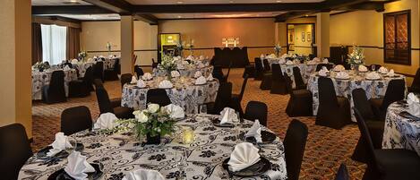 A banquet hall with multiple round tables set for dining, each with white tablecloths and black chairs.