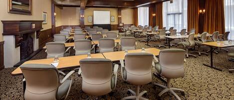 A conference room with rows of chairs and tables, a projector screen, and a fireplace.