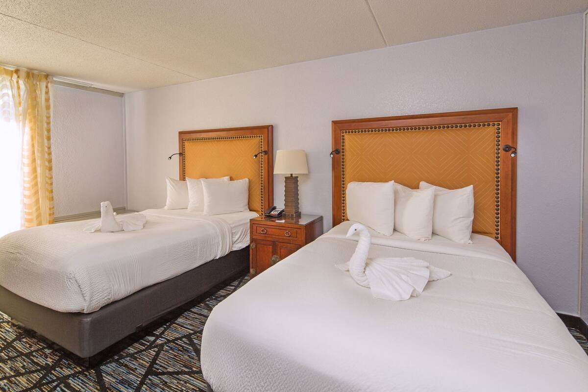 A hotel room with two beds, each with a wooden headboard, white bedding, and a towel shaped like a swan.