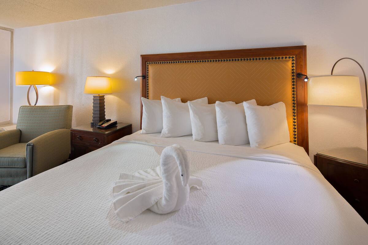 A hotel room with a large bed, a wooden headboard, a chair, a nightstand, and two lamps.