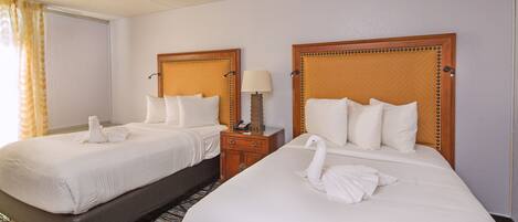 Two single beds with wooden headboards, white linens, and a bedside table with a lamp.