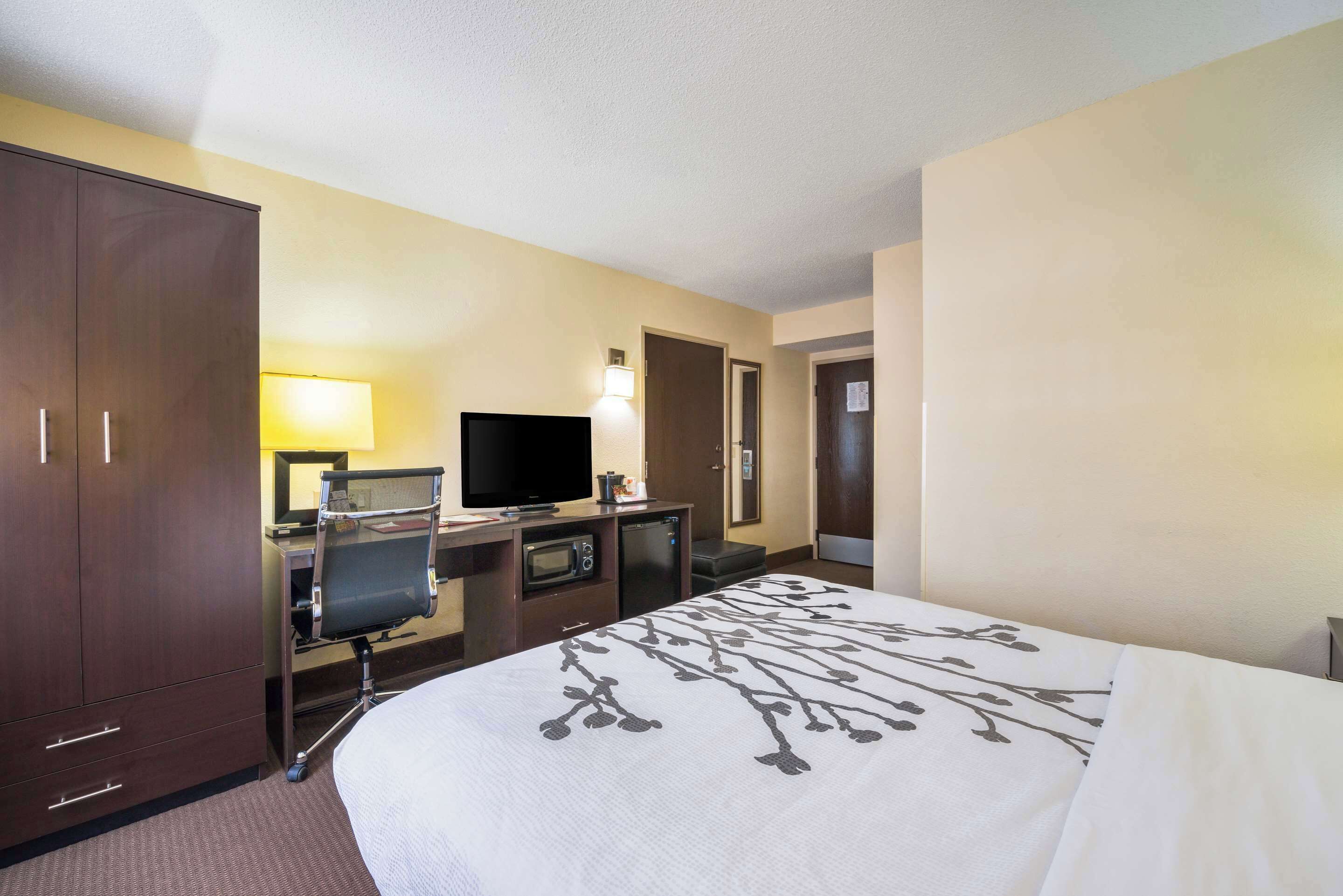 A hotel room with a bed, a desk with a computer, a television, and a minibar.