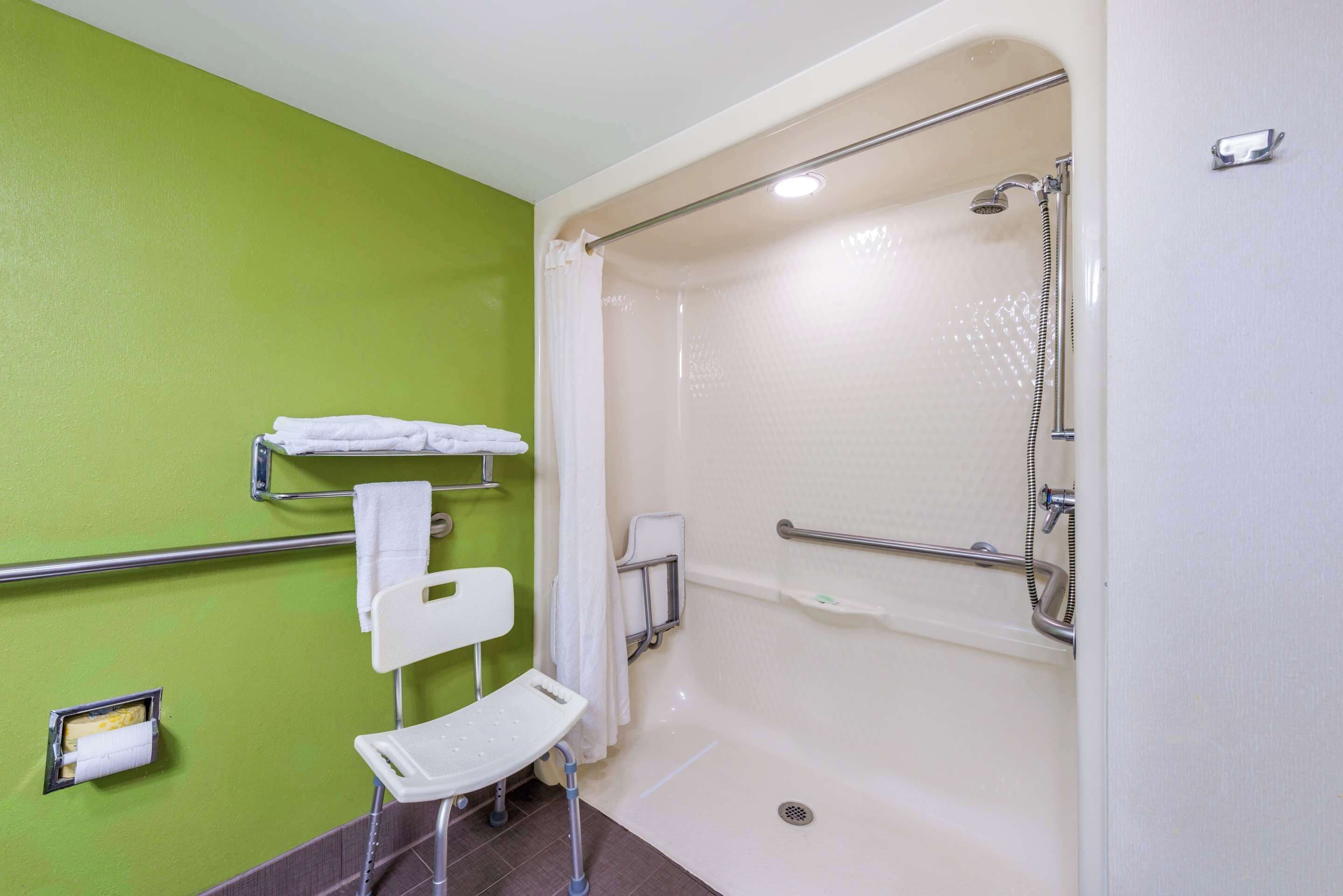A bathroom with a green wall, a white bathtub, a shower area, a white chair, and a towel rack.