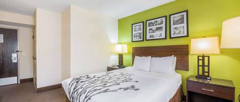 A hotel room with a large bed, two bedside tables with lamps, a wooden headboard, and green walls.