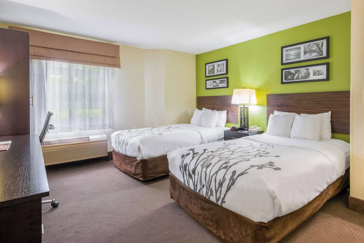 Ein Hotelzimmer mit zwei Betten, einem Schreibtisch, einem Fenster mit Vorhängen und einer Wand mit gerahmten Bildern.
