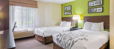 Habitación de hotel con dos camas, un escritorio, una ventana con cortinas y una pared con cuadros.