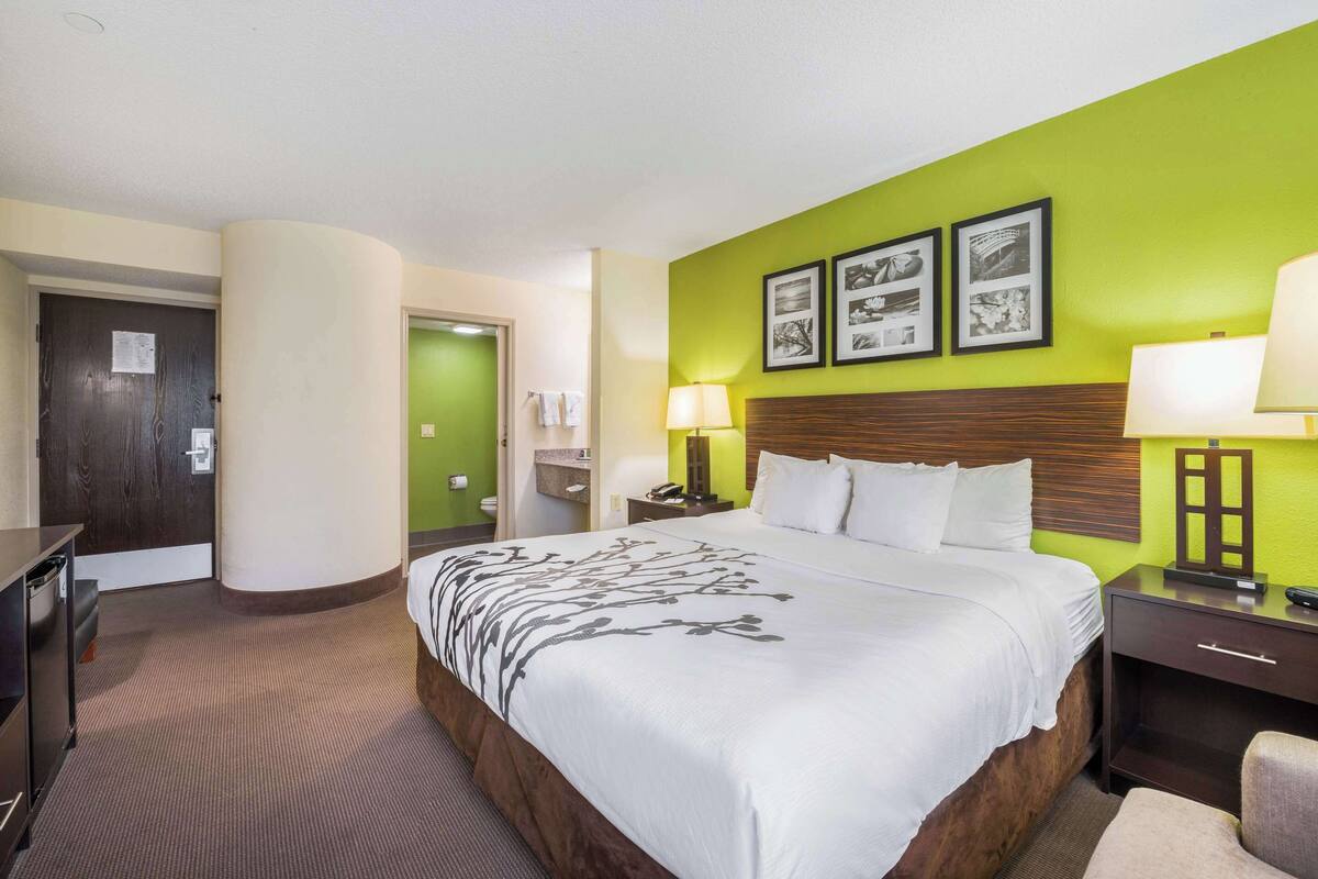 Ein Hotelzimmer mit einem großen Bett, einem Nachttisch, einer Lampe und einer Wand mit gerahmten Bildern.