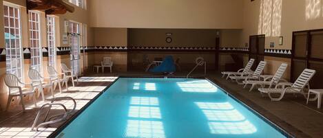 Une piscine intérieure à l’eau claire, entourée de murs baignés de lumière et dotée d’un sol carrelé.