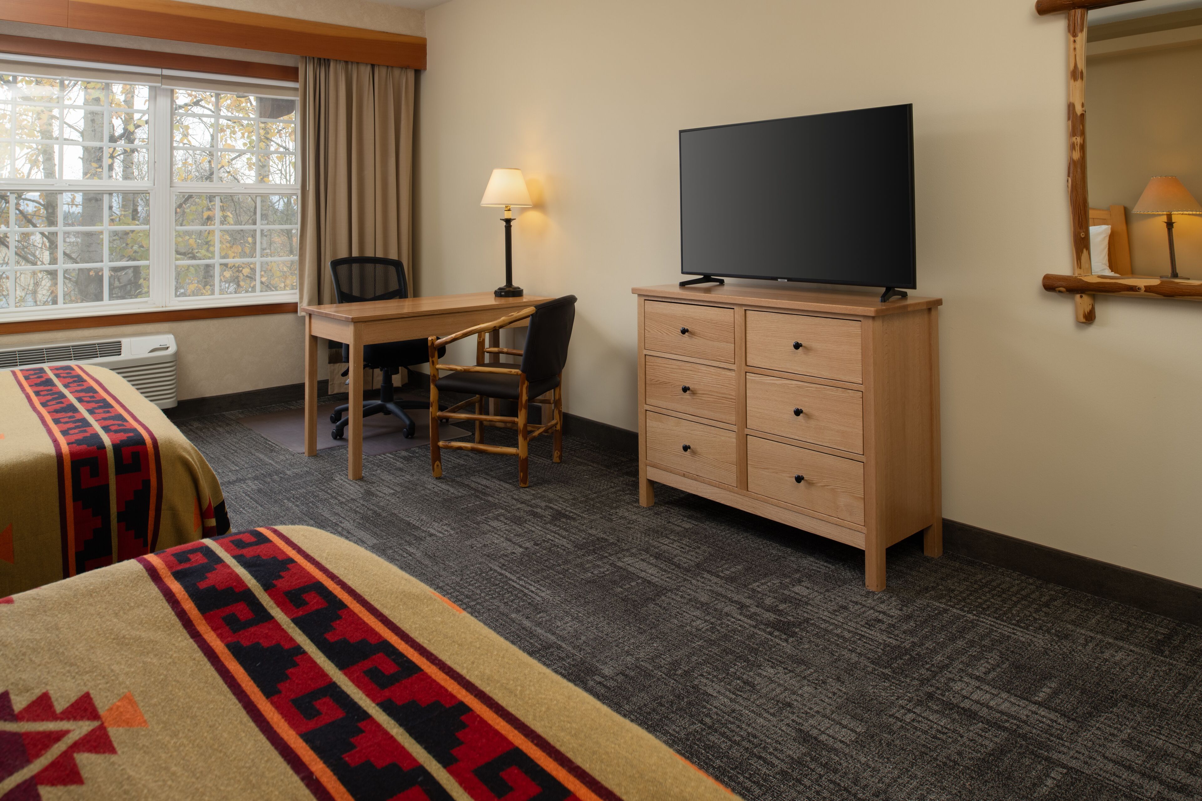 A hotel room with a bed, a desk, a chair, a TV, and a dresser.
