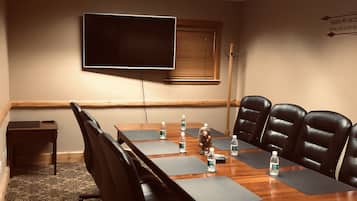 A conference room with a long table, black leather chairs, water bottles, a flat-screen TV, and a window with blinds.