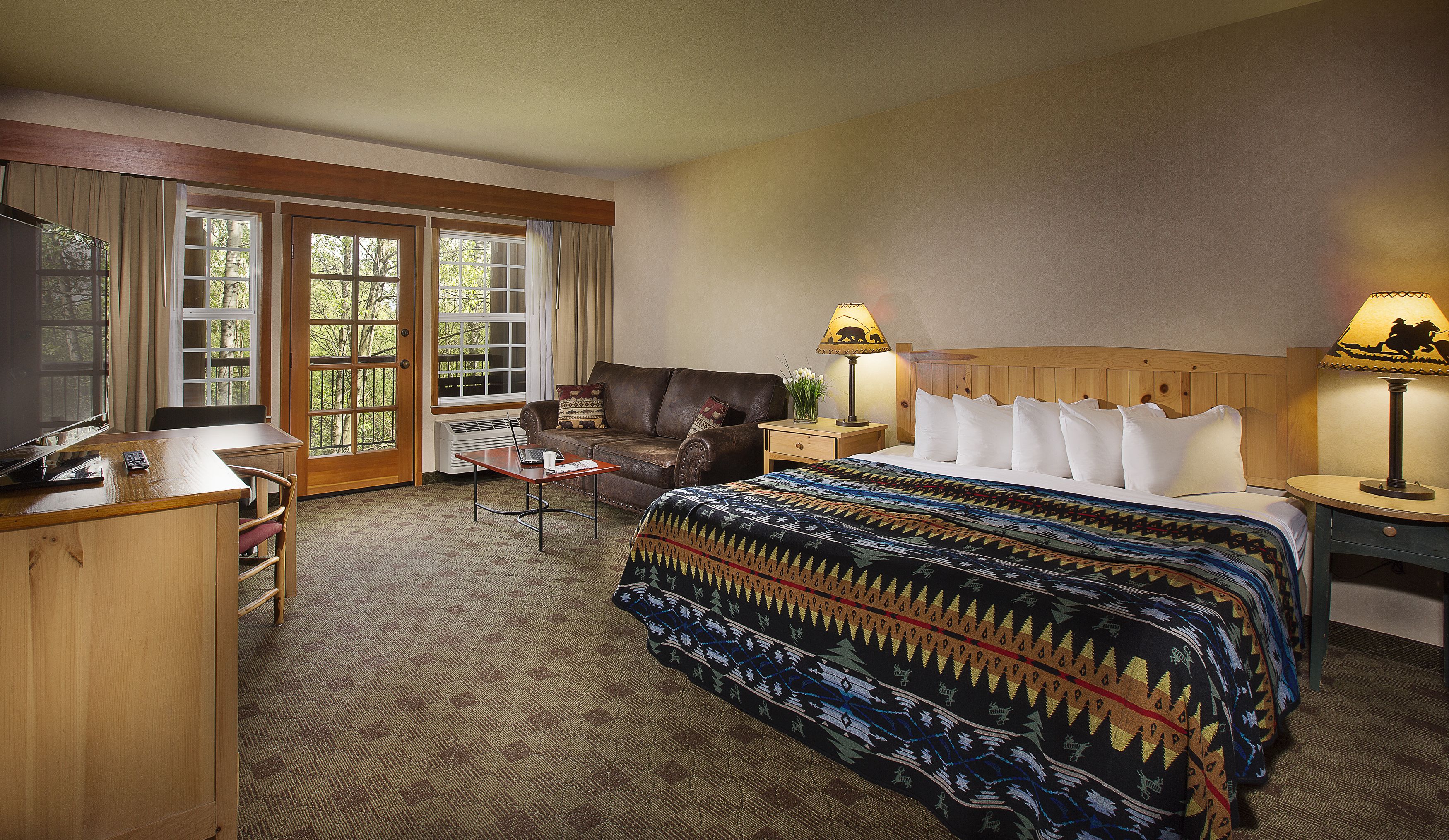 A hotel room with a bed, a desk with a laptop, a chair, a sofa, and a TV.