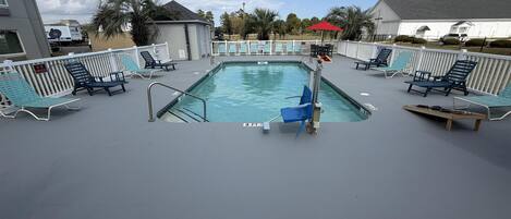 A pool area with lounge chairs, a pool ladder, and a white fence.