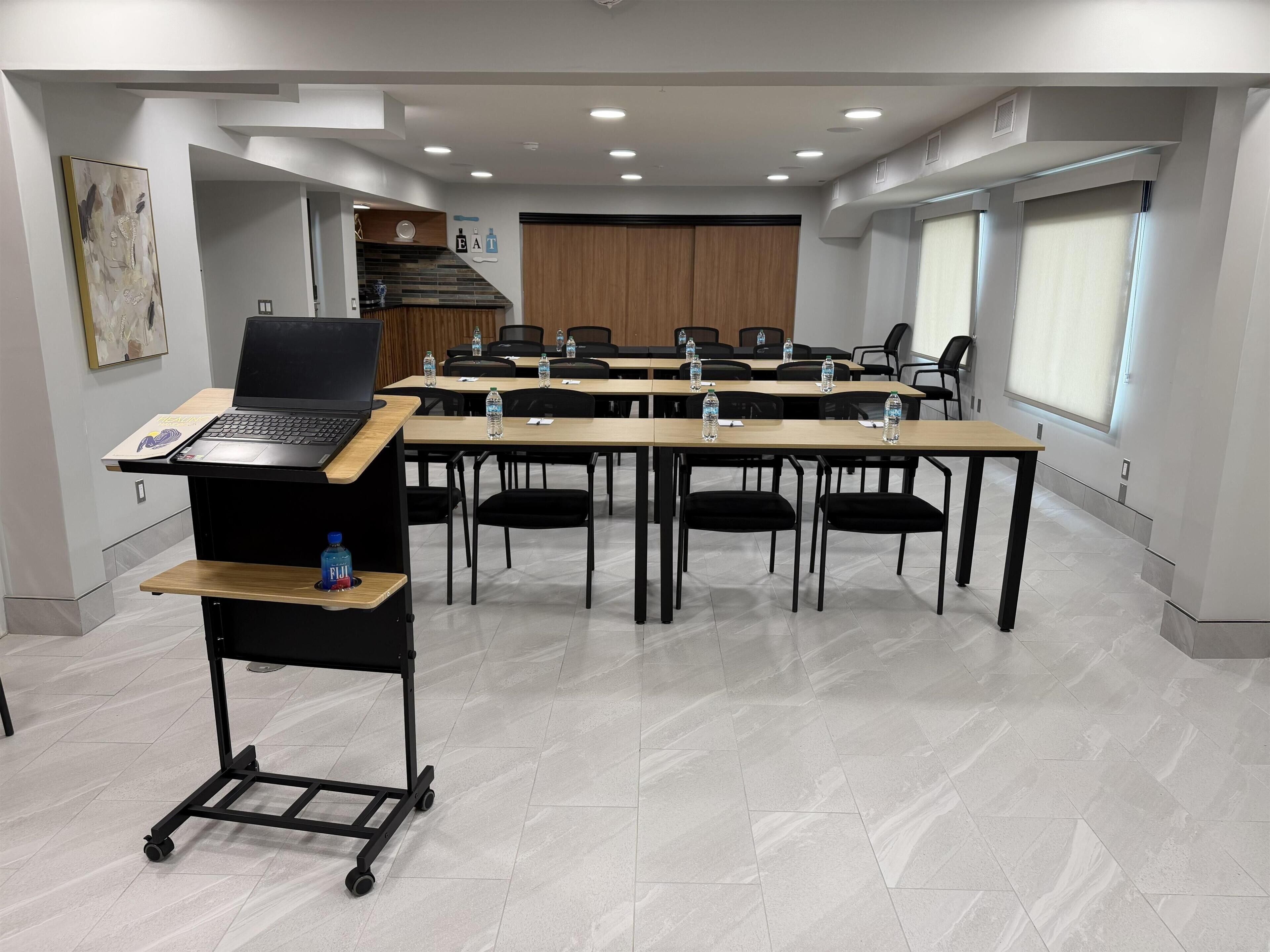 Uma sala de conferências com um laptop em um carrinho, garrafas de água sobre as mesas e uma janela grande.