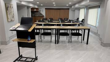 A conference room with a laptop on a cart, water bottles on tables, and a large window.