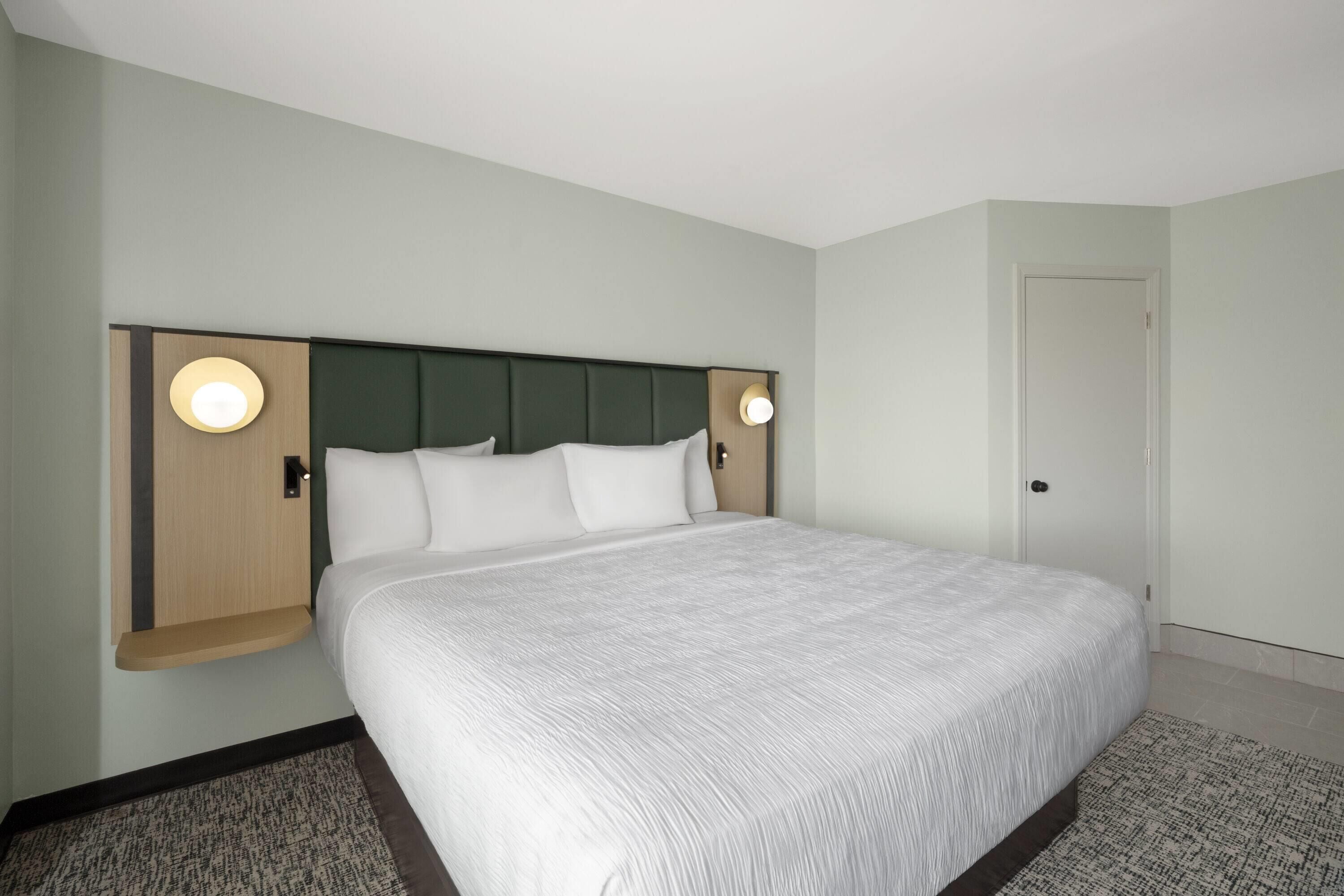 Ein Hotelzimmer mit einem großen Bett, zwei Nachttischen, einem Kopfteil und zwei Wandlampen.