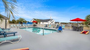 A pool area with lounge chairs, umbrellas, and a building with a steeple in the background.