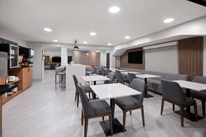 A modern dining area with tables and chairs, a kitchen area, and a television.