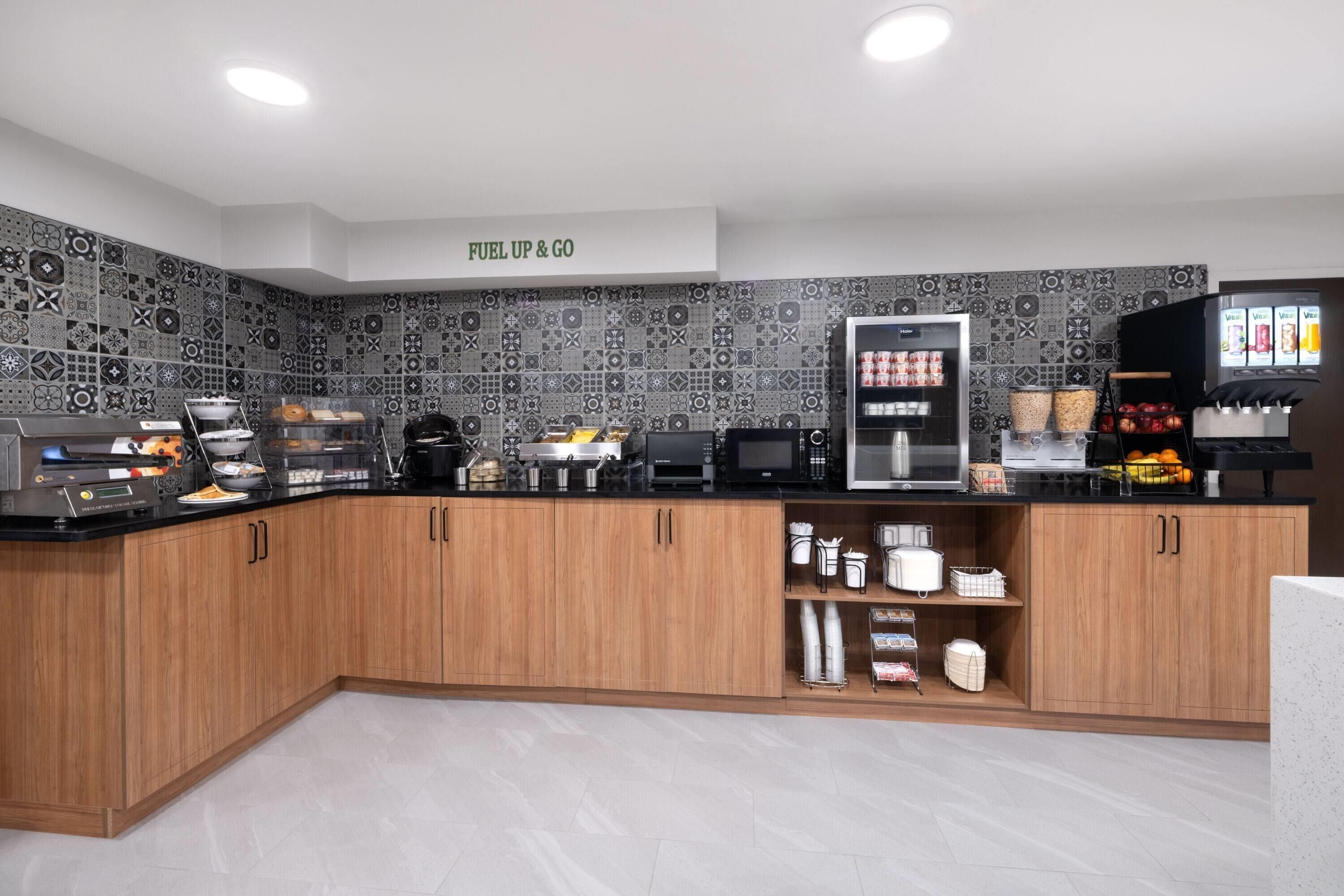 A modern kitchen with a patterned backsplash, a coffee station, and a refrigerator stocked with beverages.