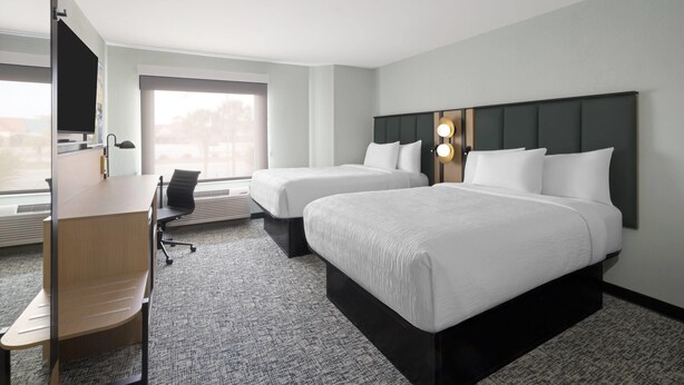 A hotel room with two beds, a desk, a chair, and a large window.