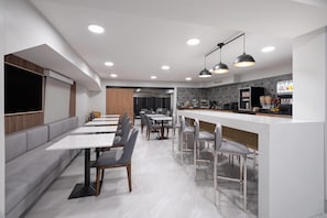 A modern restaurant with a long counter, multiple seating areas, and a kitchen in the background.