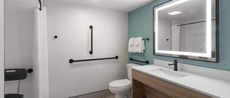 Un baño moderno con inodoro blanco, lavamanos con espejo y zona de ducha.