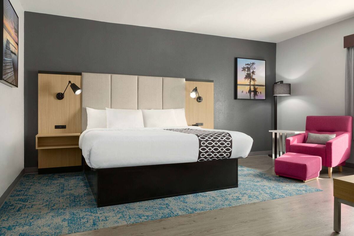 Une chambre d’hôtel moderne avec un grand lit, un fauteuil rose et une table de chevet avec une lampe.