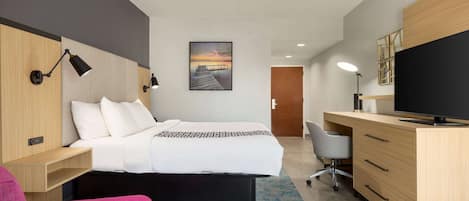 A modern hotel room with a bed, a desk with a computer, a chair, and a TV.