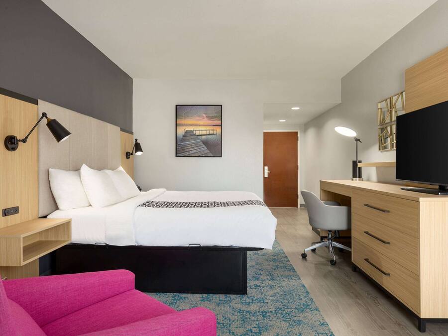 Een moderne hotelkamer met een bed, een bureau met een computer, een stoel en een televisie.