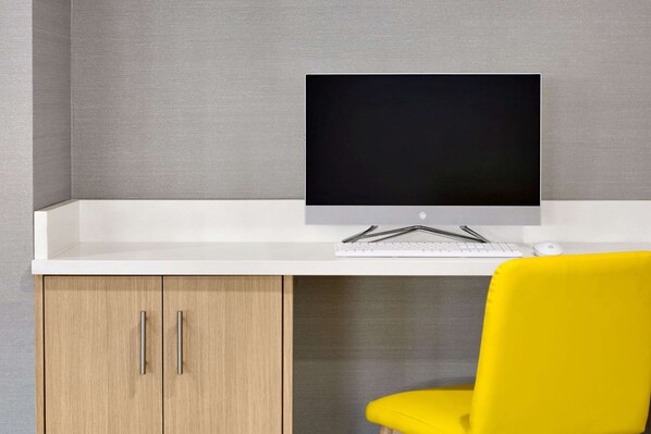 Un espacio de trabajo moderno con un escritorio blanco, un monitor de ordenador, un teclado y una silla amarilla.
