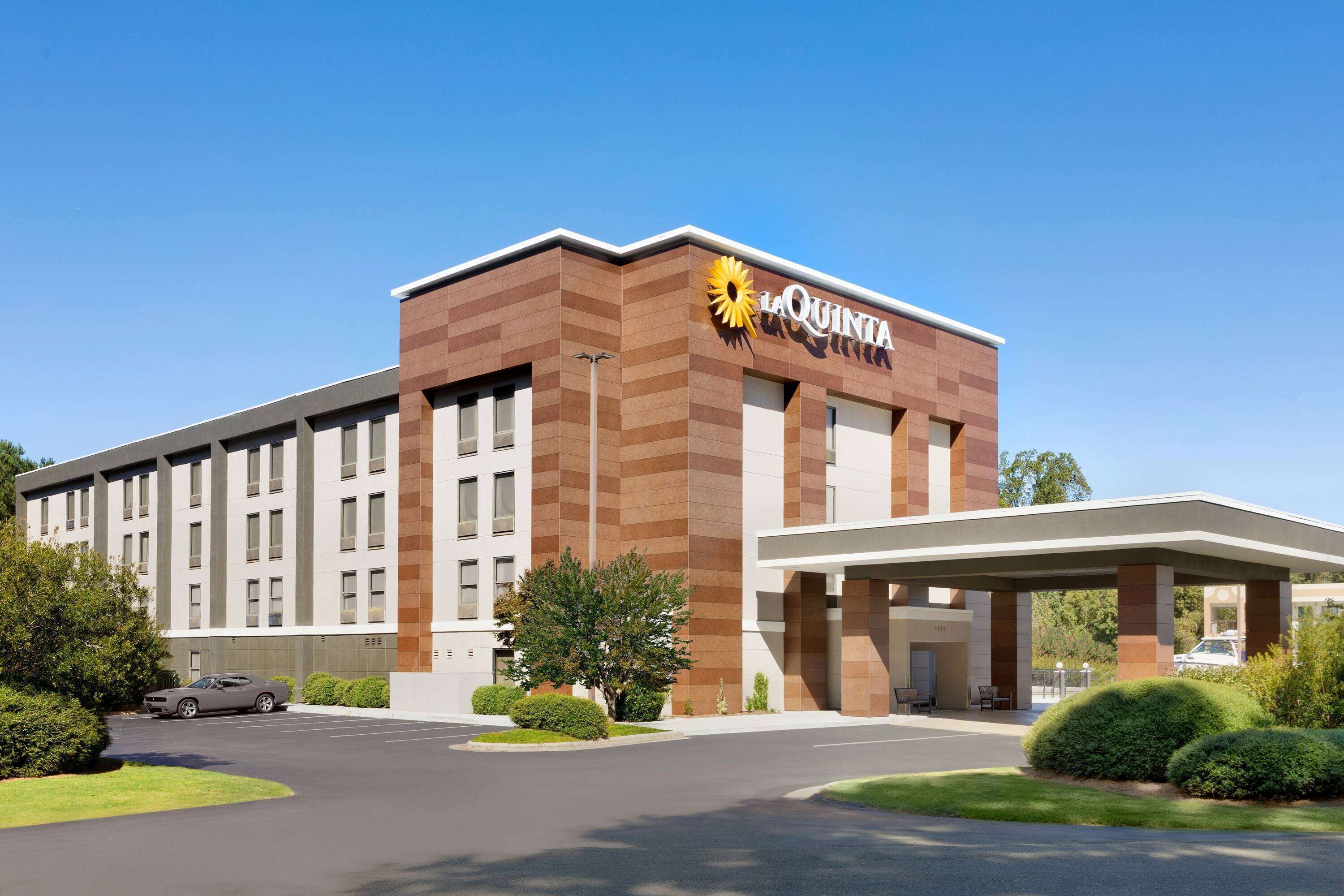 A hotel with a modern design, featuring a prominent 'La Quinta' sign, a covered entrance, and a parking area.