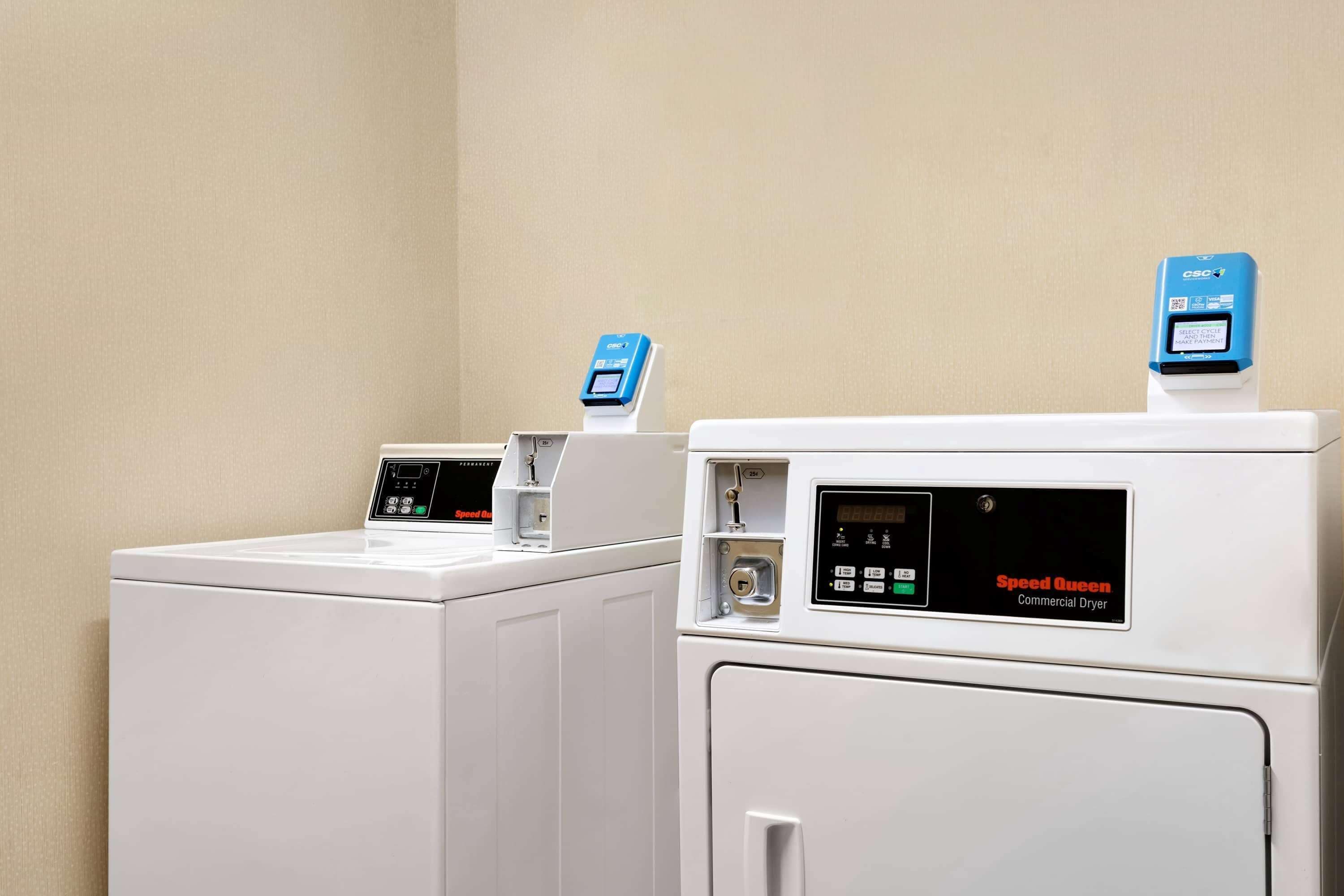 Two commercial dryers, Speed Queen, in a laundry room with beige walls.