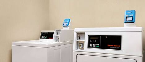 Two commercial dryers, Speed Queen, in a laundry room with beige walls.