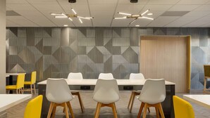 Une salle de conférence avec une longue table, des chaises blanches et un mur orné de motifs.