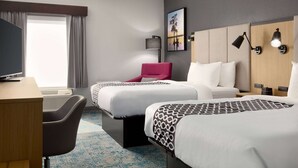 Une chambre d’hôtel avec deux lits, un bureau, une chaise, une télévision et une grande fenêtre avec des rideaux.