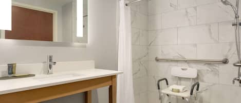 Un baño moderno con ducha, inodoro con barra de apoyo y lavamanos con espejo.