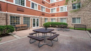 A courtyard with a picnic table, benches, and a small garden area. - Extended Stay America Suites Indianapolis West 86th St (Indianapolis)