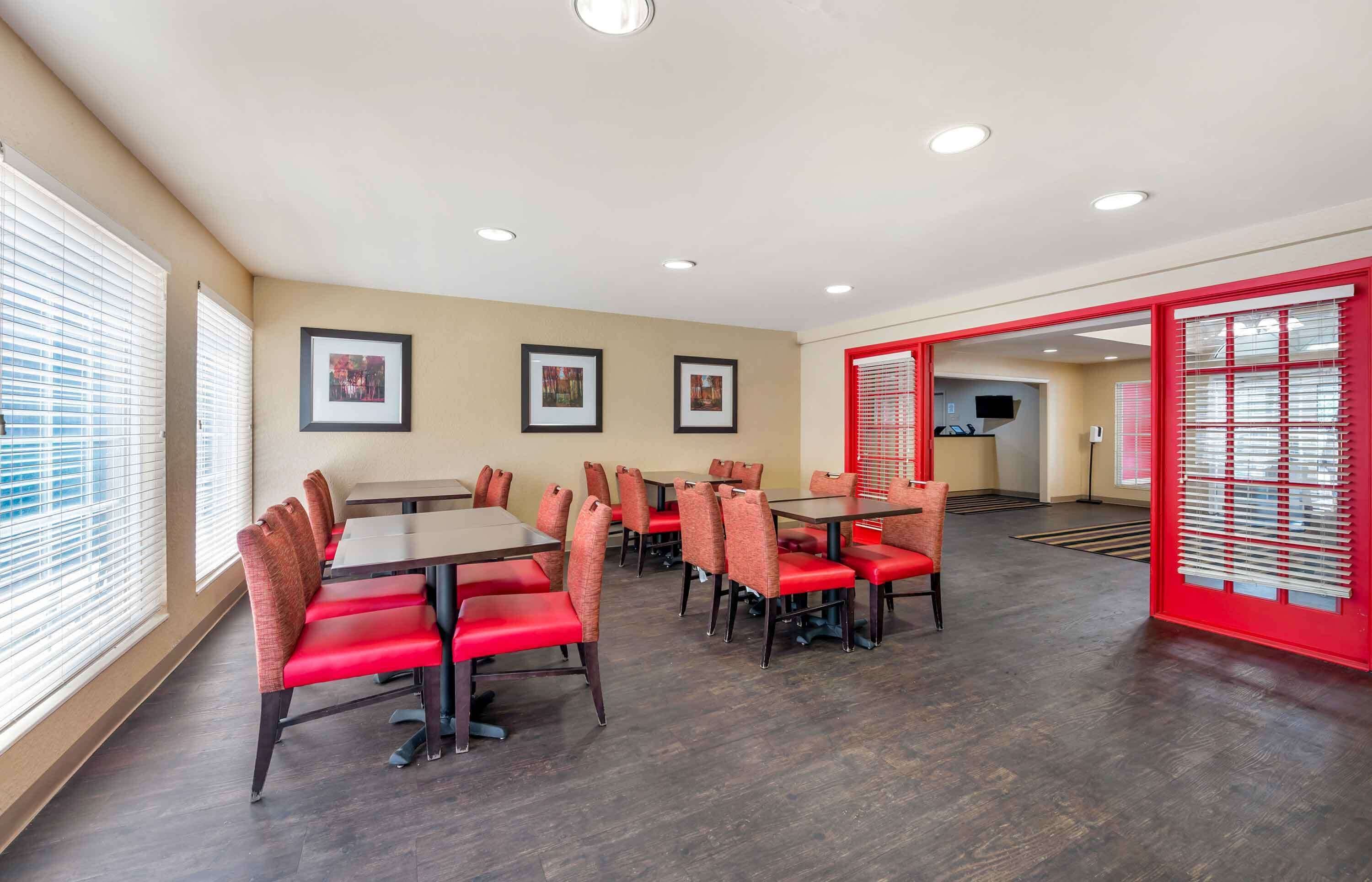 A spacious dining area with multiple tables and chairs, framed pictures on the walls, and a red-framed doorway.