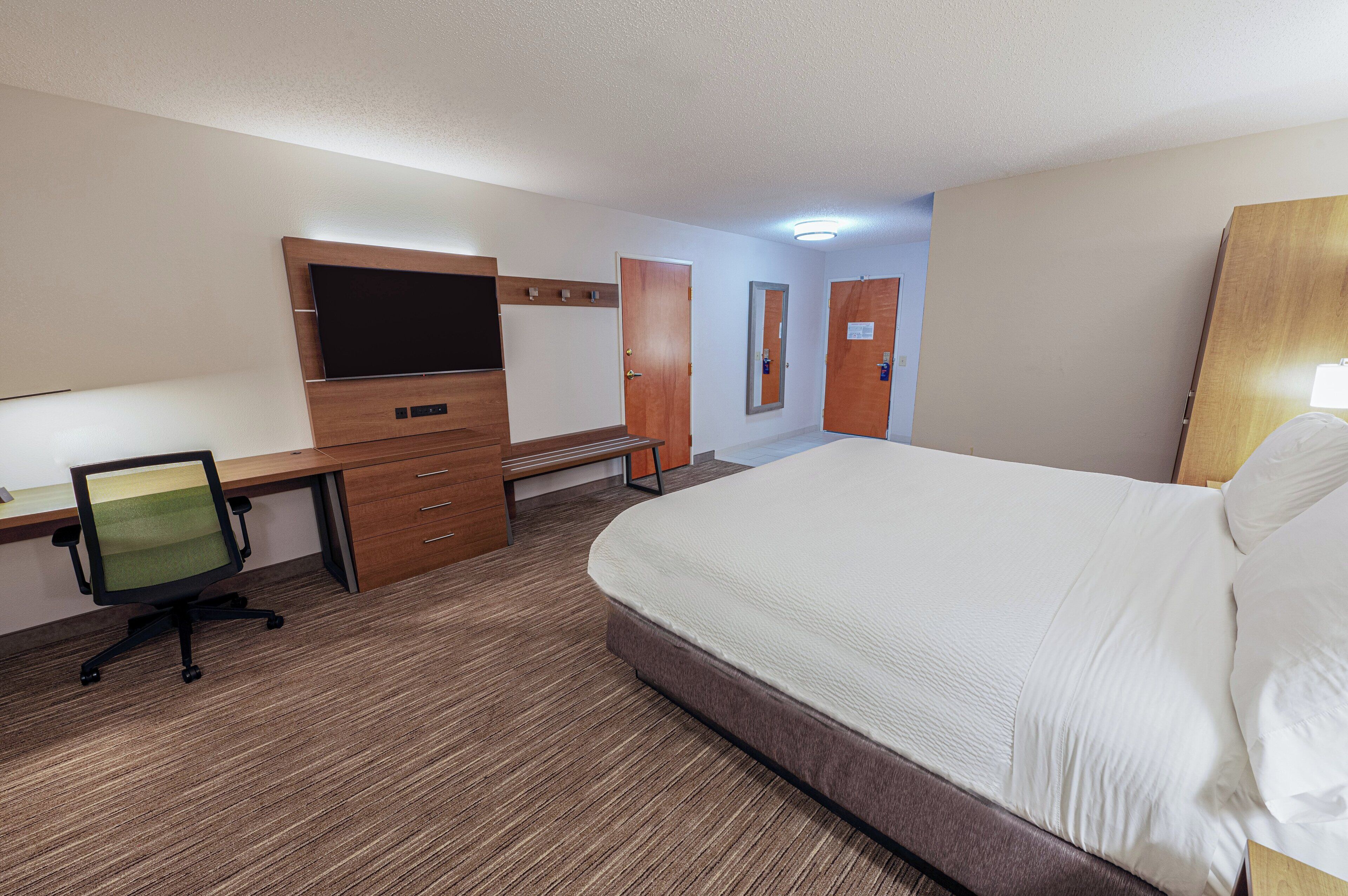 Una habitación de hotel con una cama, un escritorio con silla, un televisor y un armario.
