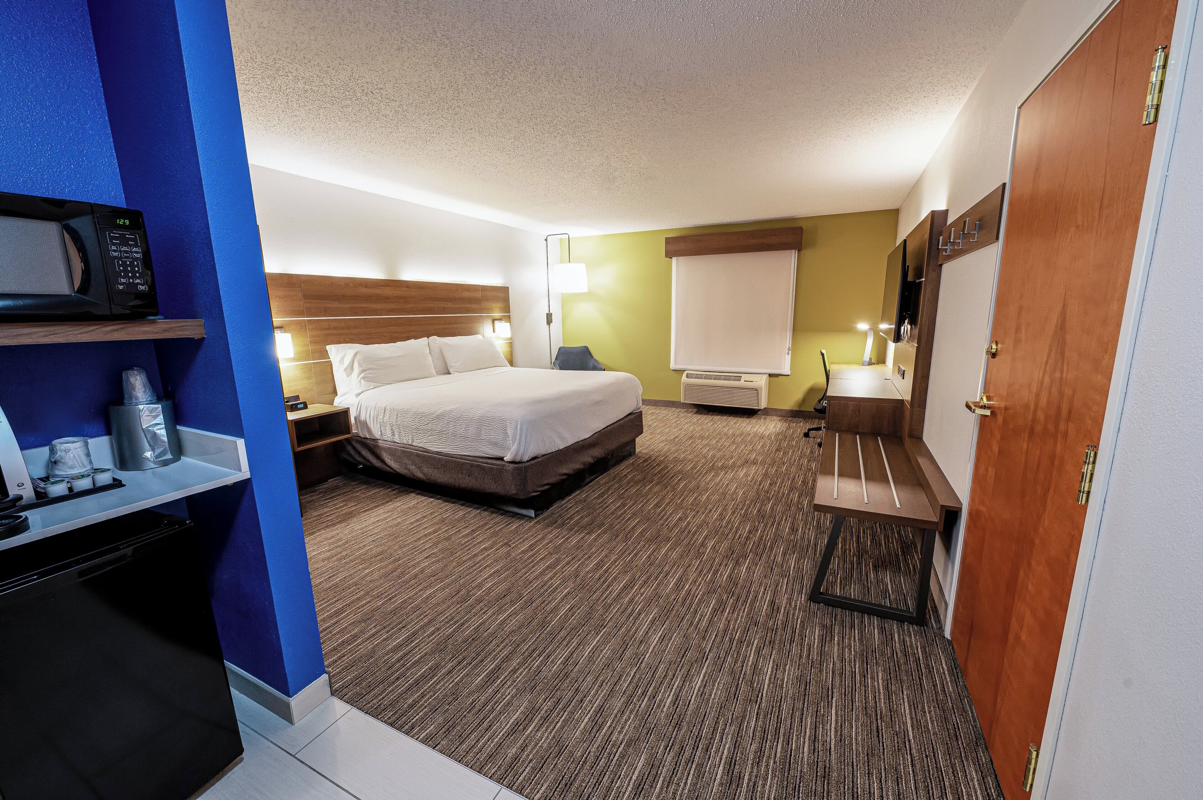 A hotel room with a bed, bedside tables, a desk with a microwave, a chair, and a wardrobe.