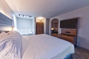A hotel room with a large bed, a flat-screen TV, a wooden dresser, a bathroom with a bathtub, and a desk with a chair. - Holiday Inn Express Hotel & Suites Goshen by IHG (Goshen)