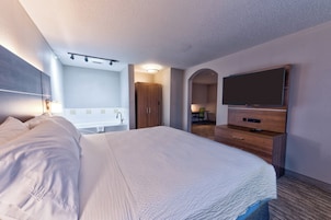 Habitación de hotel con una cama grande, un televisor de pantalla plana, un aparador de madera, un baño con bañera y un escritorio con silla.