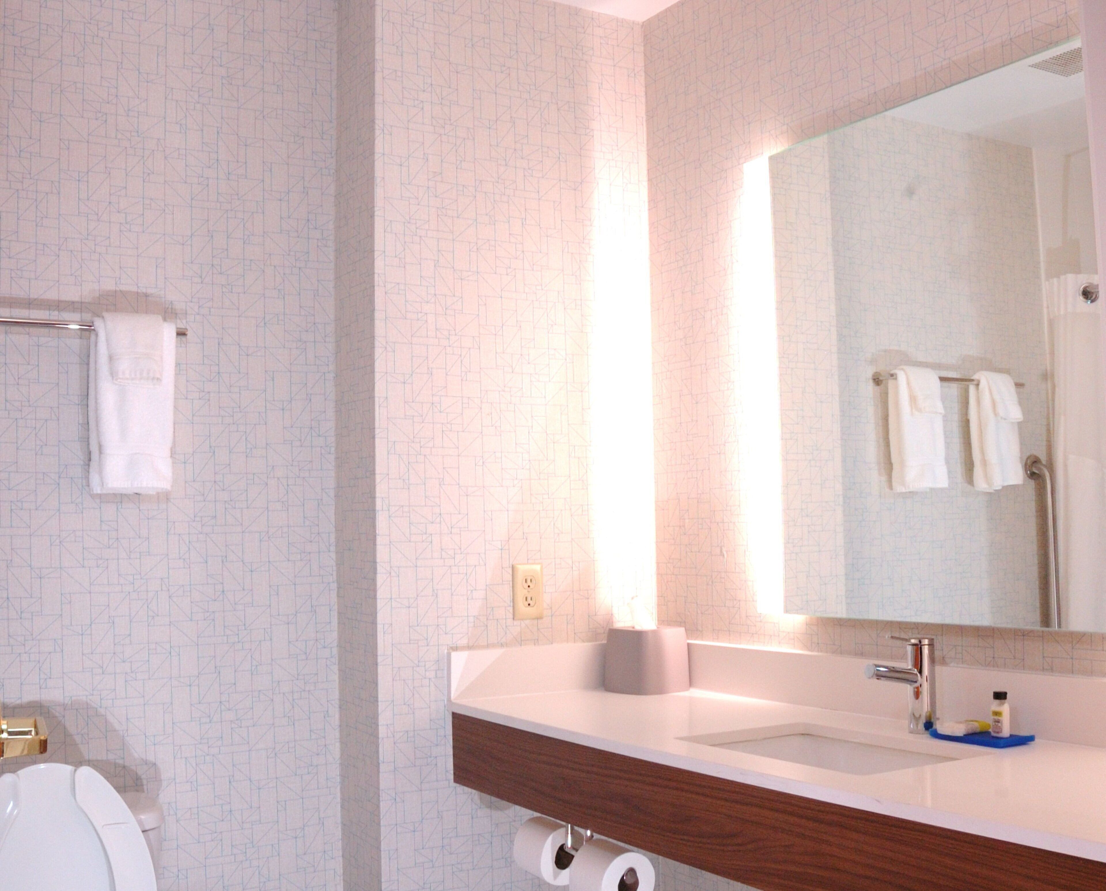 A bathroom with a white toilet, a wooden vanity with a mirror, and a towel rack.