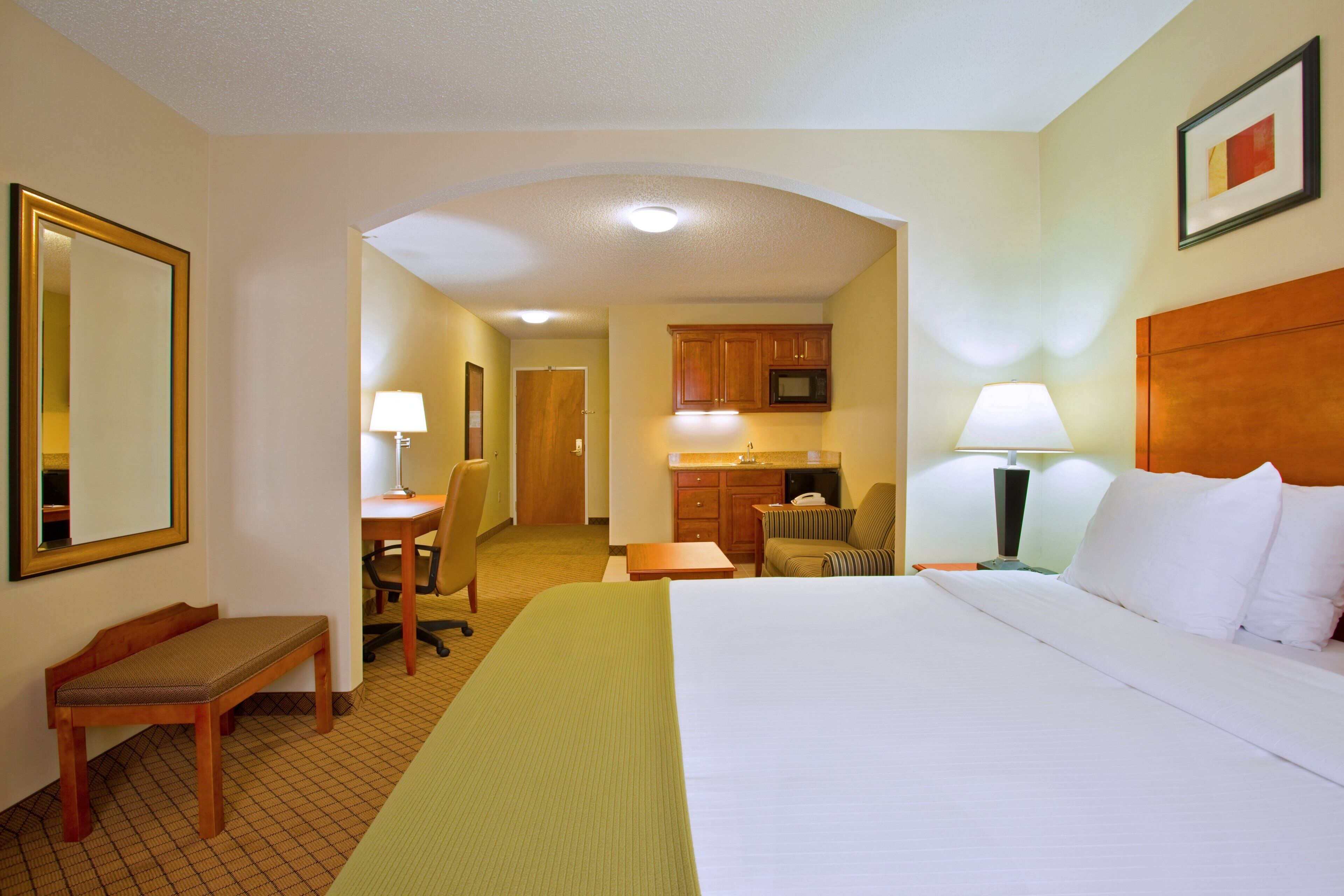 A hotel room with a bed, a desk, a chair, a small kitchenette, and a bathroom.