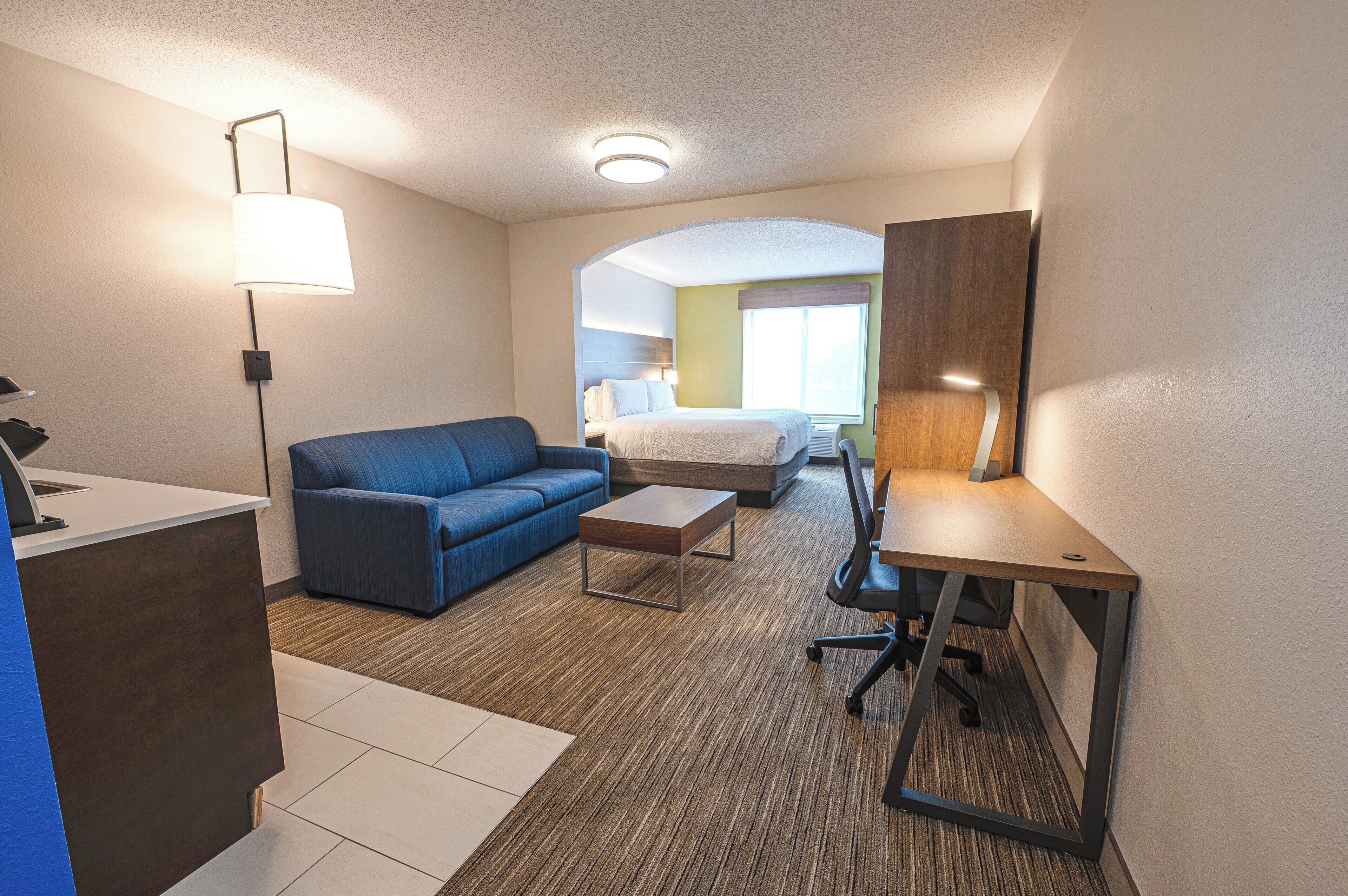 A hotel room with a bed, a blue sofa, a desk, and a lamp.